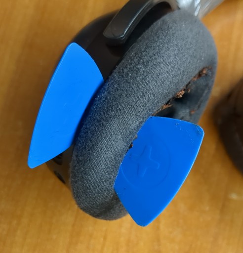 Image of the headphones with one pick inside the ear pad and one between the ear cup and ear pad