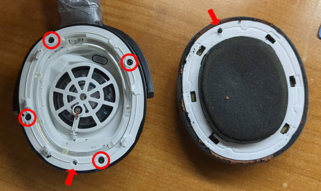 Image of the headphones with one of the ear pads removed. The removed ear pad is laying next to it. There are four Phillips screws marked with a circle in the speaker